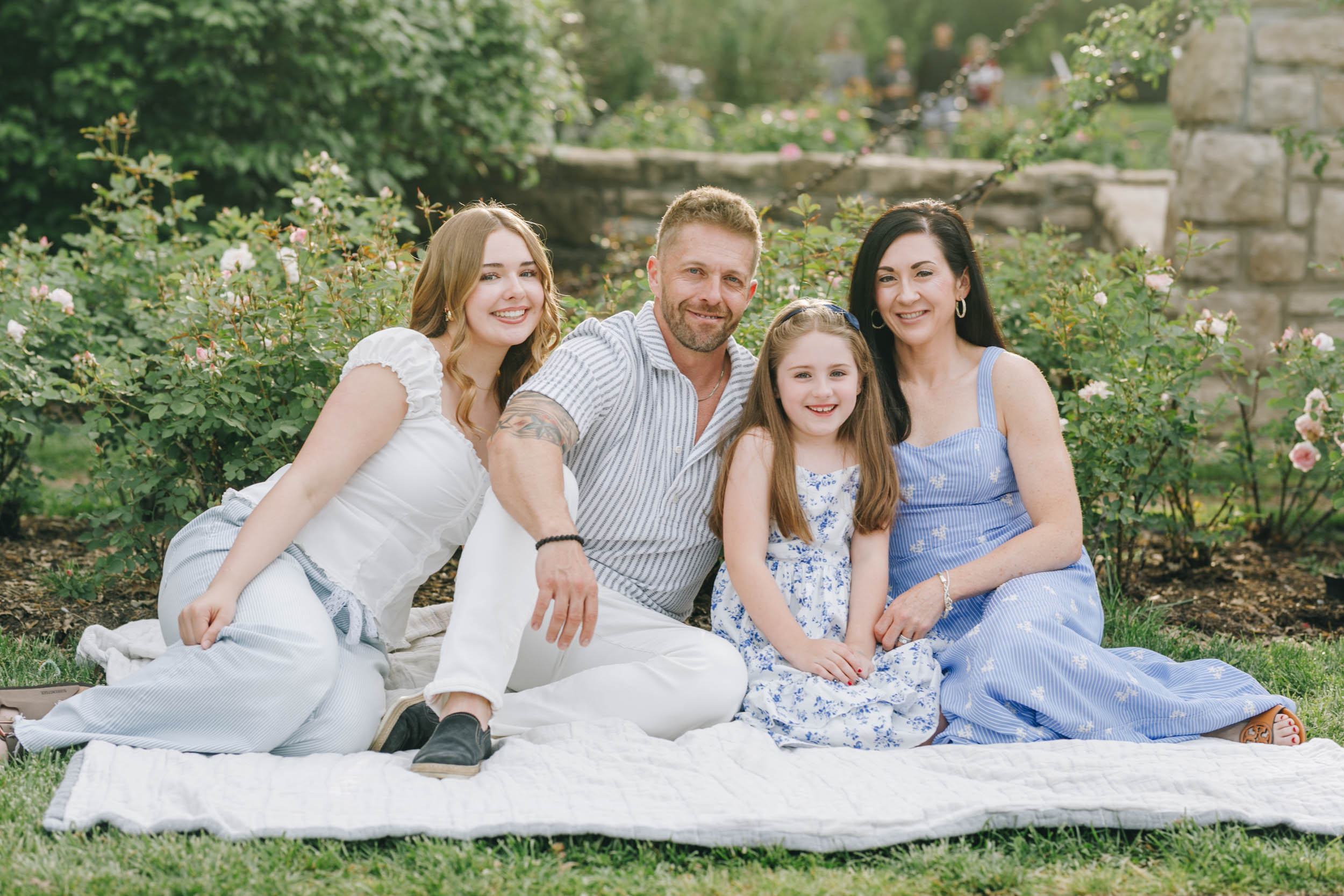 family sitting in front of rose bushes at loose park photographed by kymberly janelle photography
